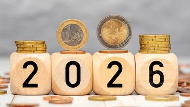 Holzwürfel mit der Jahreszahl 2026 und darauf liegenden Euro-Münzen