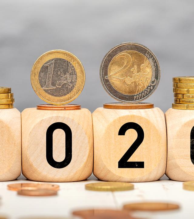 Holzwürfel mit der Jahreszahl 2026 und darauf liegenden Euro-Münzen