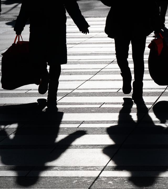 Symbolbild: Passanten mit Einkaufsbeuteln zeichnen sich im Gegenlicht als Silhouette ab. 