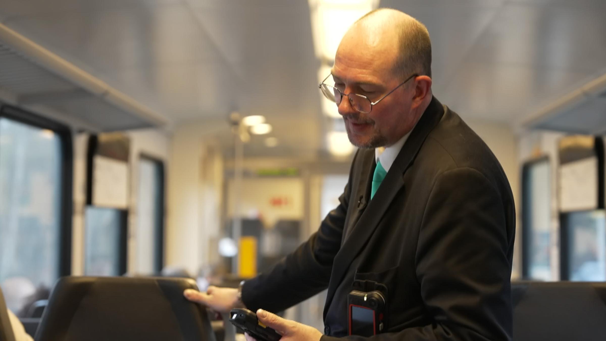 Ein Zugbegleiter kontrolliert Reisende in einer Bahn.