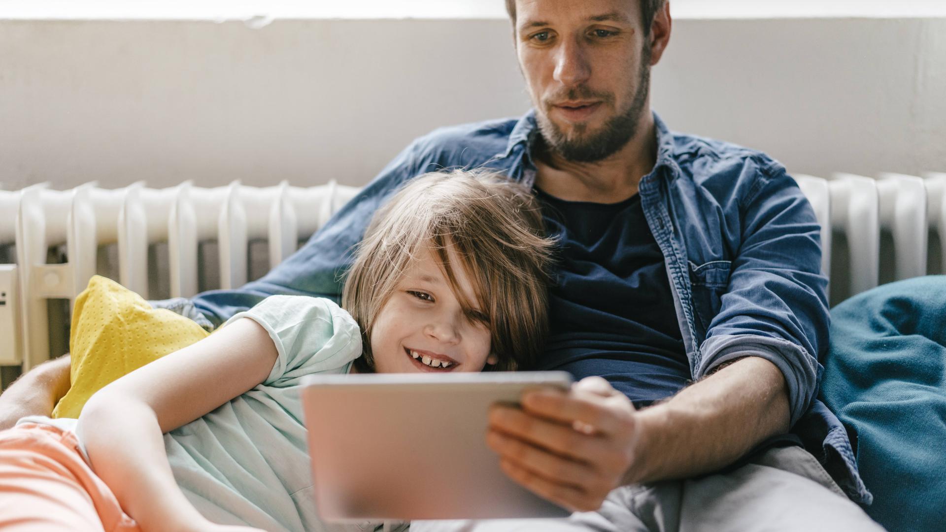Mann sitzt neben Kind und hält ein IPad in der Hand