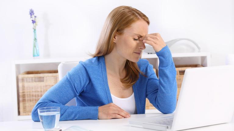 Eine Frau vor ihrem Laptop stützt ihren Kopf ab.