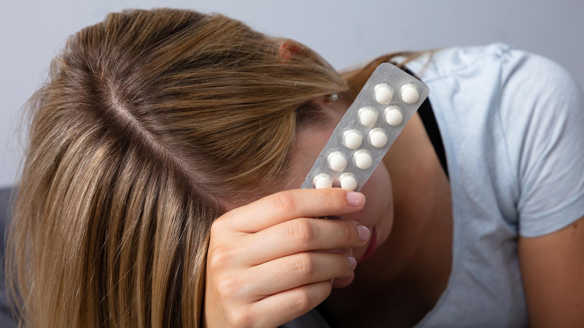 Frau mit Kopfschmerzen hält Tabletten in der Hand