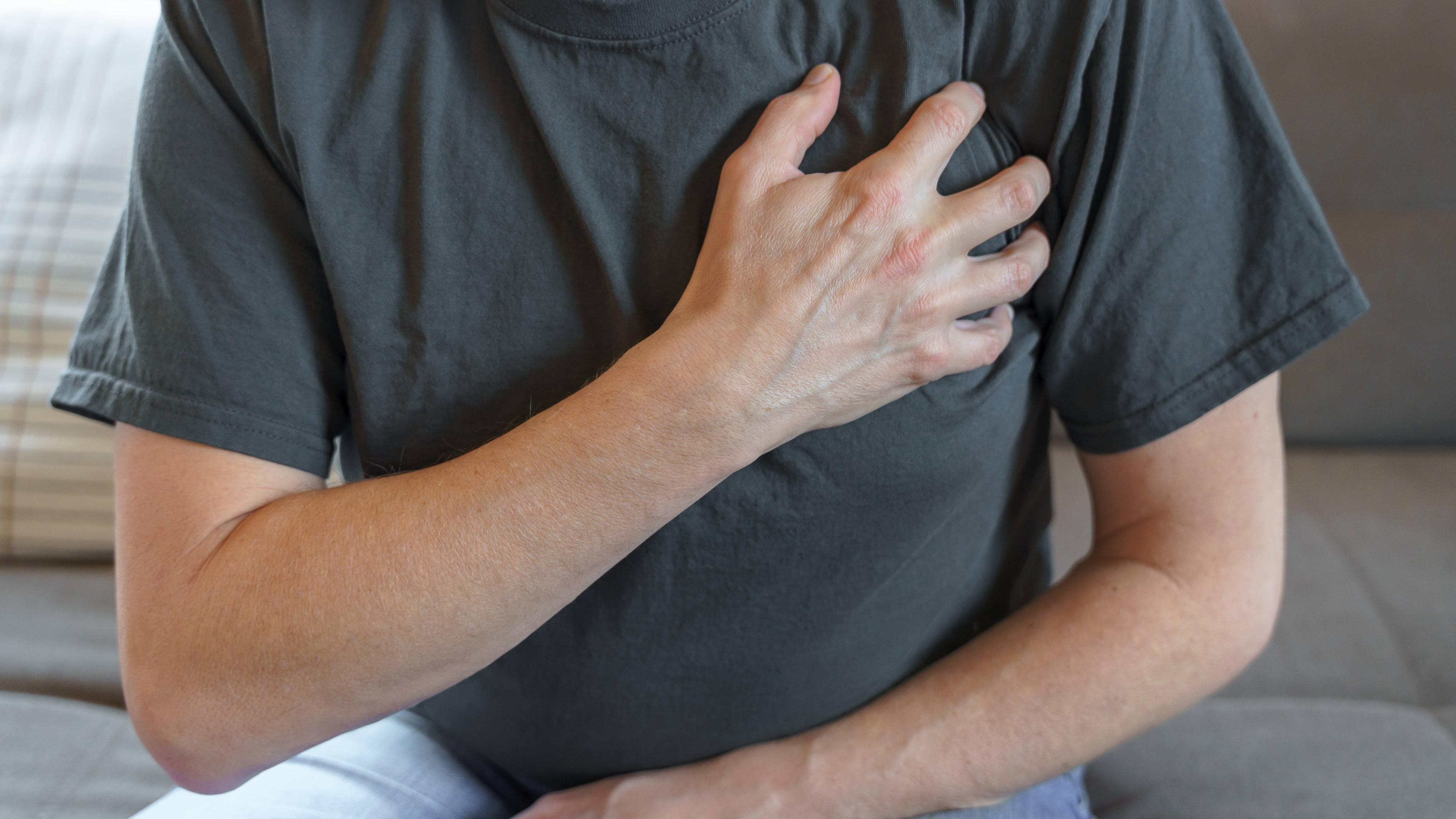 Ein Mann in einem grauen T-Shirt greift sich an die Brust.