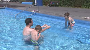 Kinder spielen mit ihrem Vater im Wasser im Freibad.