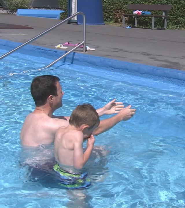 Kinder spielen mit ihrem Vater im Wasser im Freibad.