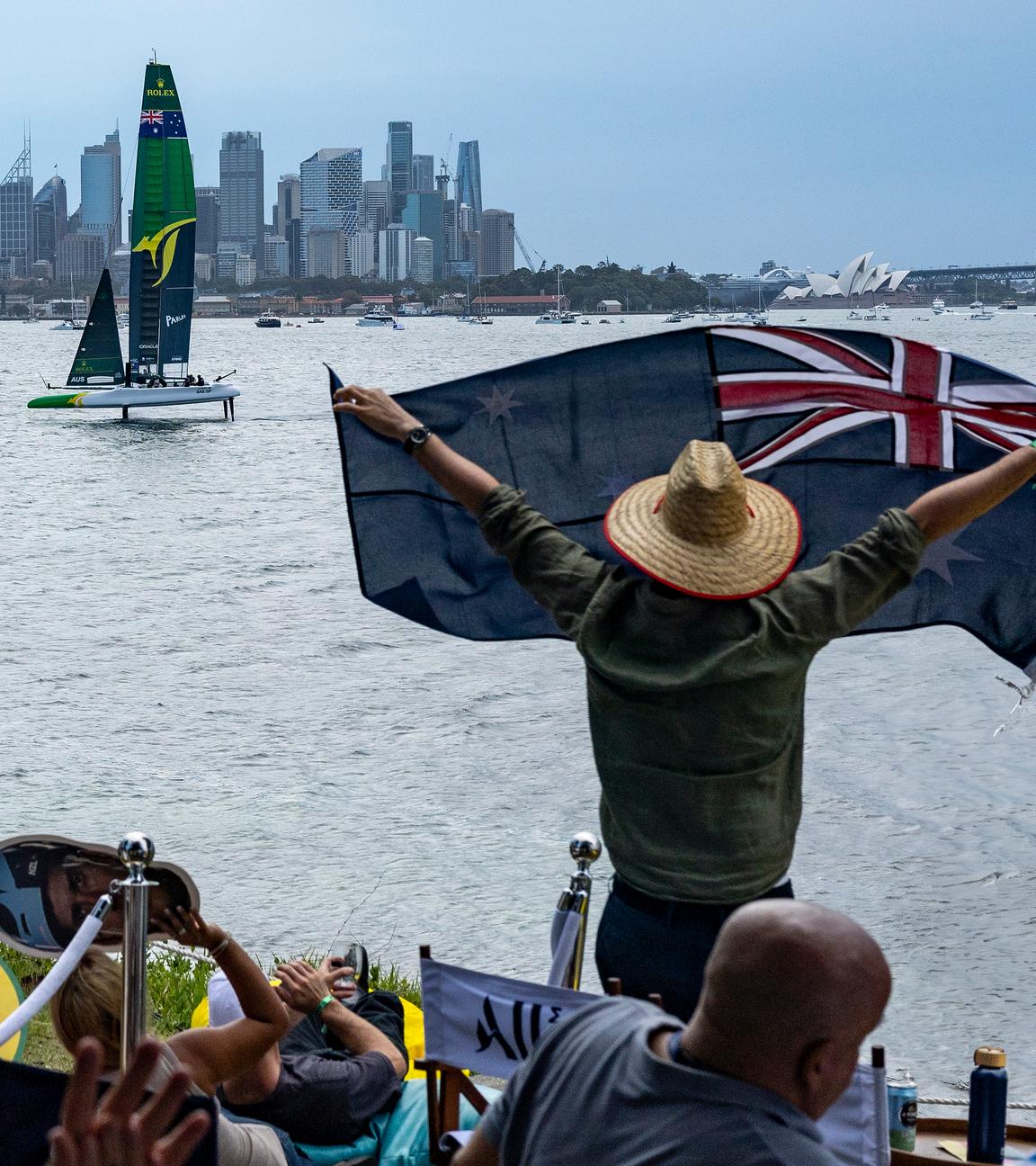 Australien, Sydney: Zuschauer schwenken Fahnen und winken, während sie das Rennen von Shark Island aus verfolgen.