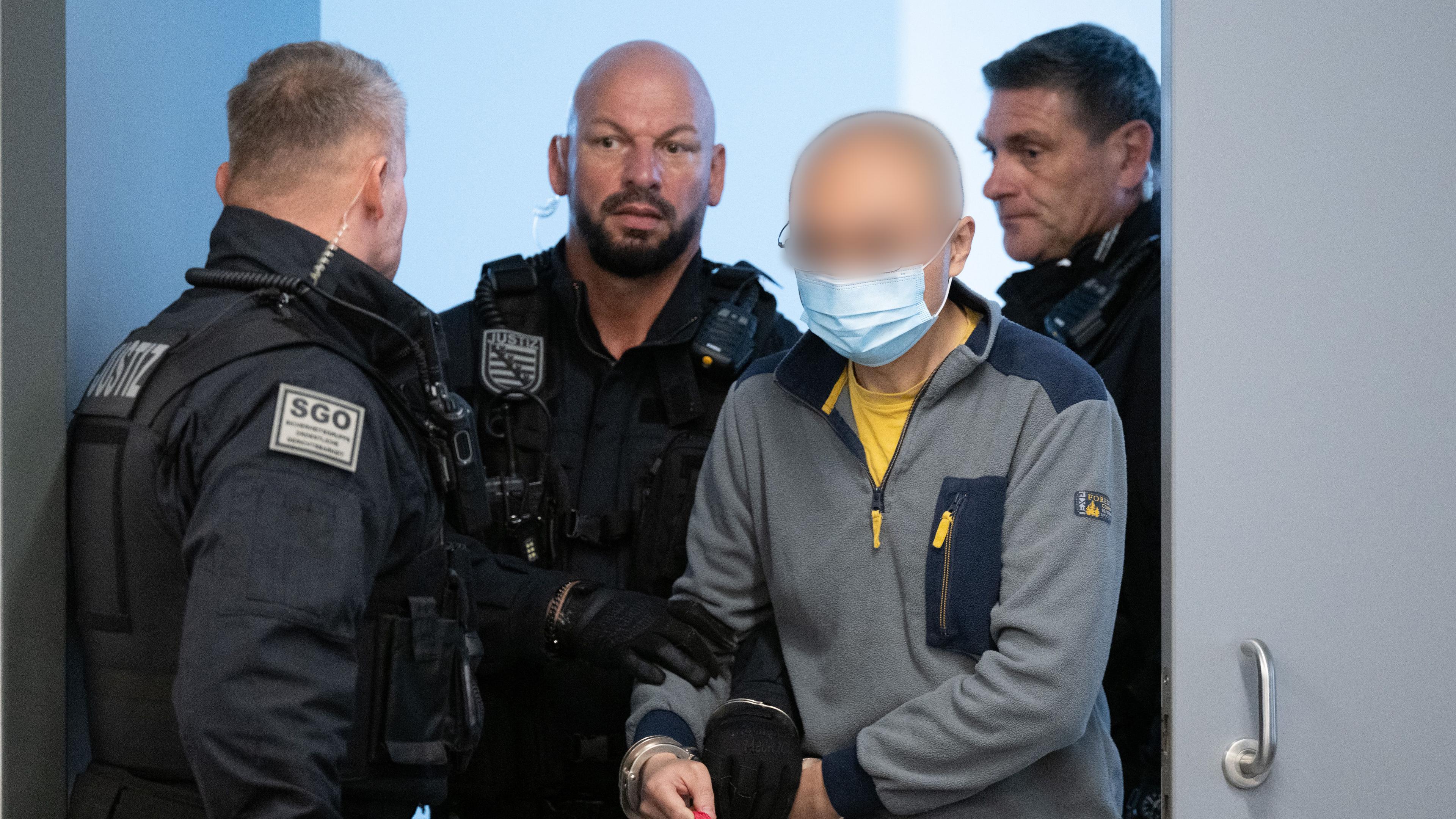 05.08.2025, Sachsen, Dresden: Der Hauptangeklagte Jian G. (2.v.r.) wird vor Prozessbeginn in den Gerichtssaal geführt.
