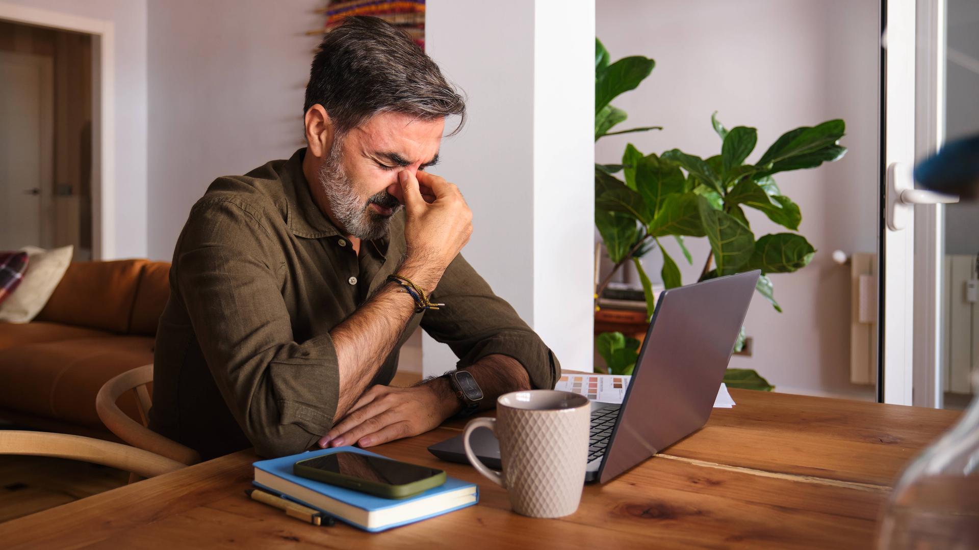Ein Mann, der sich sichtbar nicht wohlfühlt, sitzt vor dem Laptop im Homeoffice.