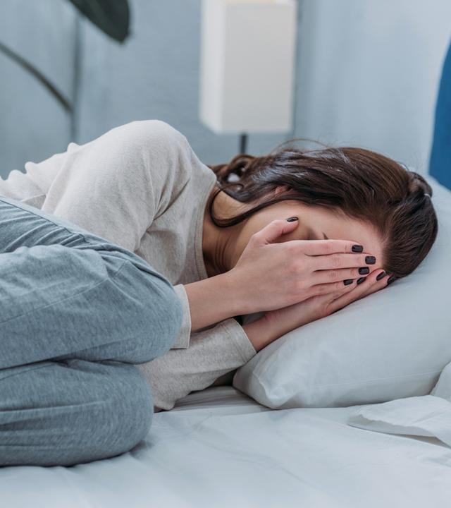 Depressive Frau liegt weinend im Bett und bedeckt Gesicht mit Händen (Symbolfoto)
