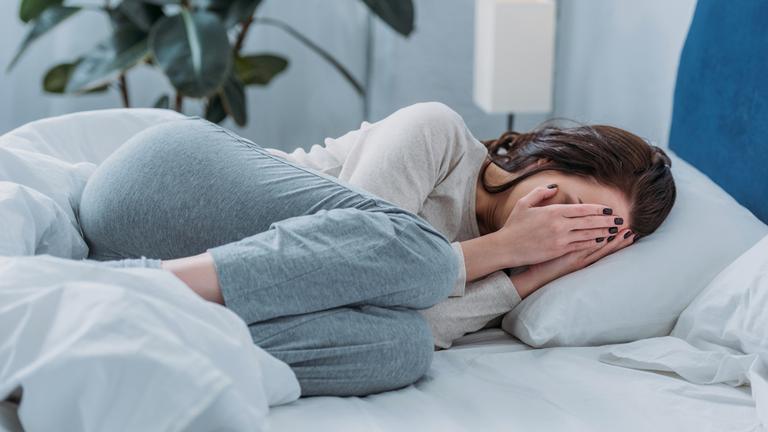 Depressive Frau liegt weinend im Bett und bedeckt Gesicht mit Händen (Symbolfoto)