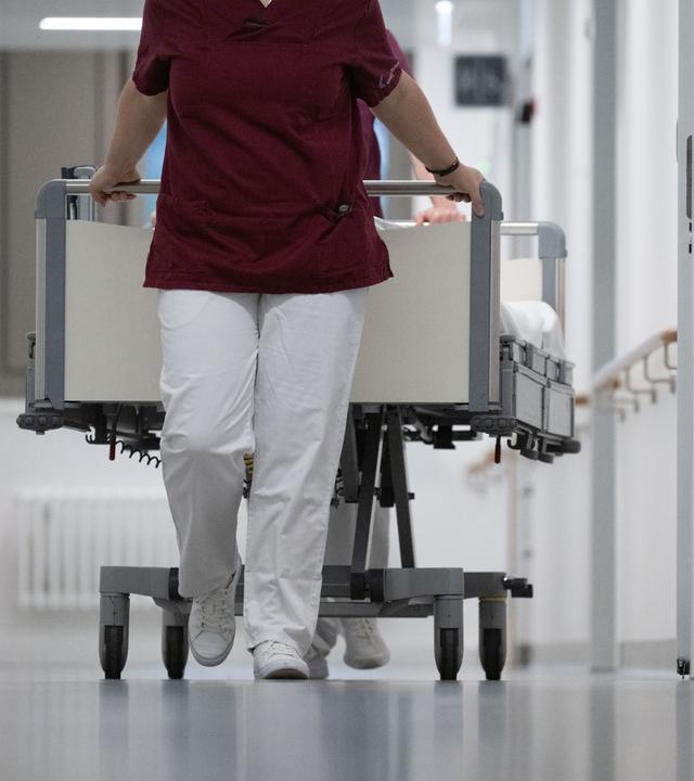Pflegekraft zieht ein Krankenbett durch den Gang eines Krankenhauses