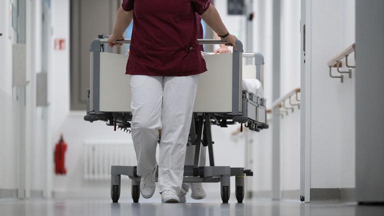 Pflegekraft zieht ein Krankenbett durch den Gang eines Krankenhauses