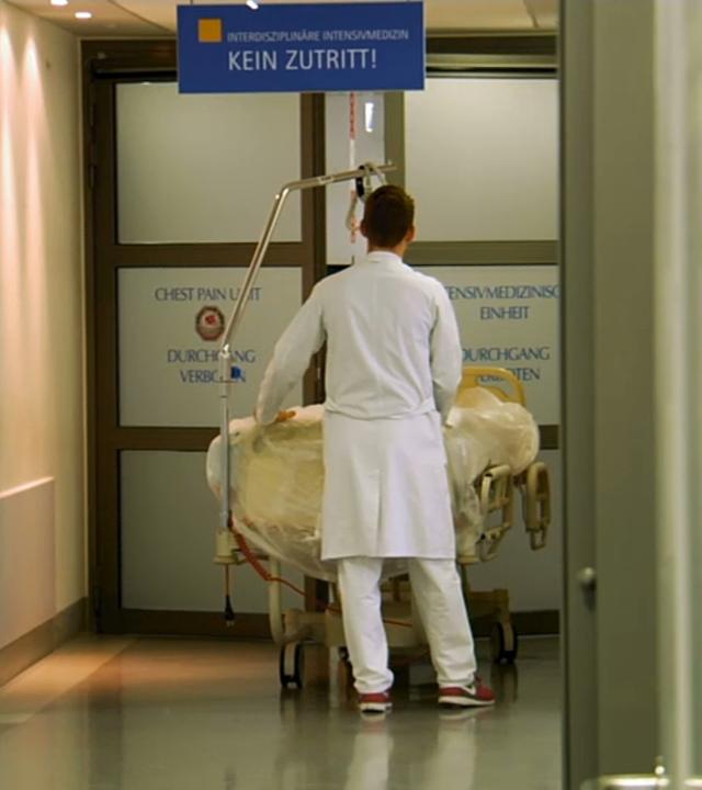 Ein Arzt schiebt ein Bett in einem Krankenhausflur durch eine automatische Tür auf die Intensivstation.