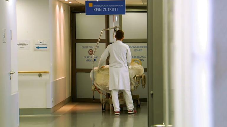 Ein Arzt schiebt ein Bett in einem Krankenhausflur durch eine automatische Tür auf die Intensivstation.