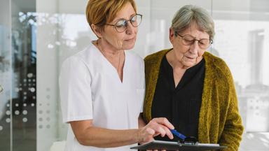 Eine Patientin und eine Mitarbeiterin eines Krankenhauses schauen in eine Akte.