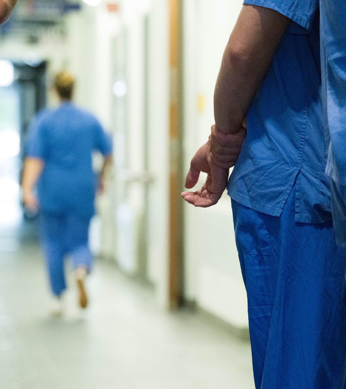 In einem Gang im Krankenhaus befinden sich mehrere Pflegende in blauer Arbeitskleidung.