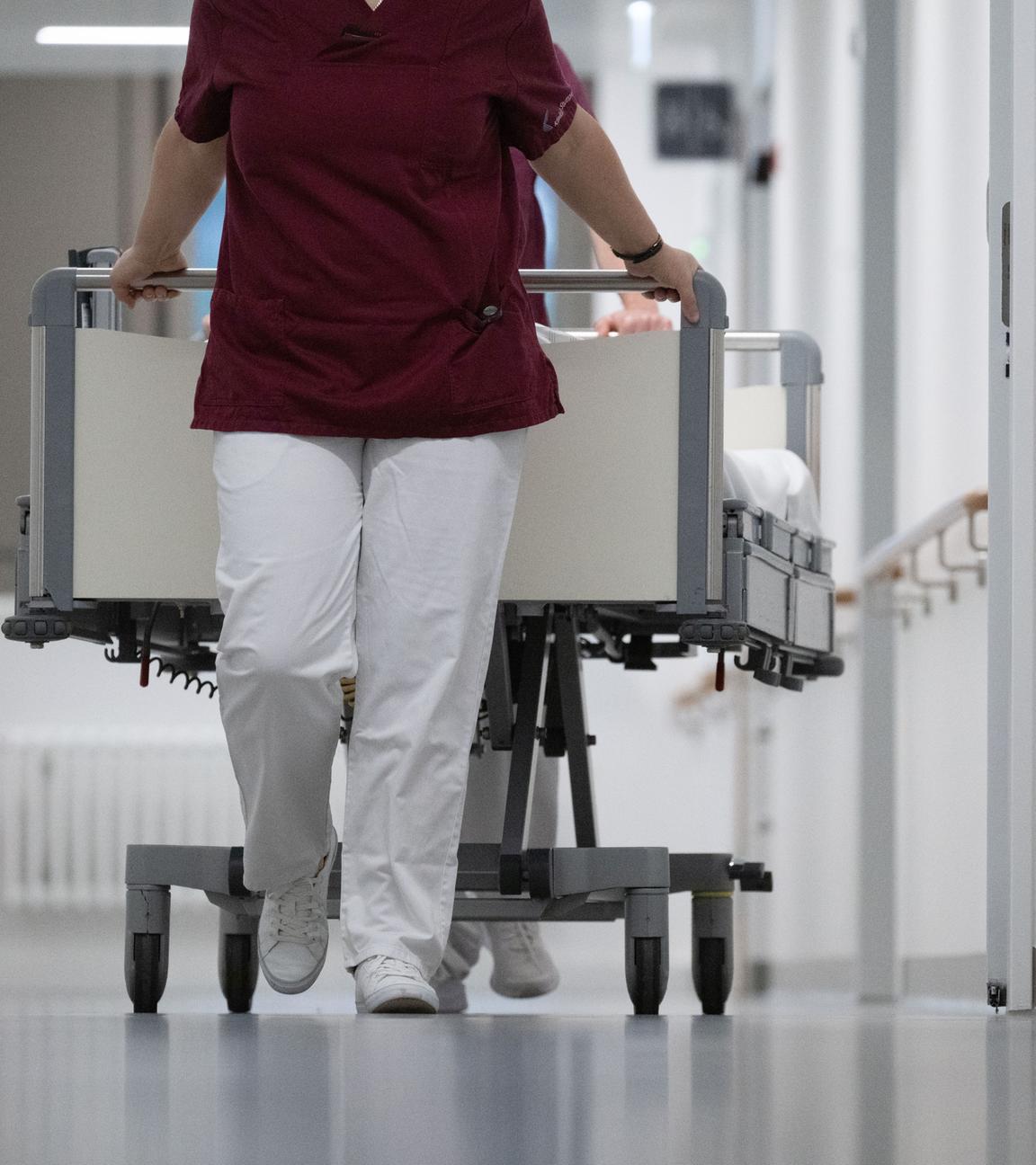 Baden-Württemberg, Stuttgart: Eine Krankenpflegerin und ein Krankenpfleger schieben ein Krankenbett durch den Gang einer Station eines Krankenhauses.