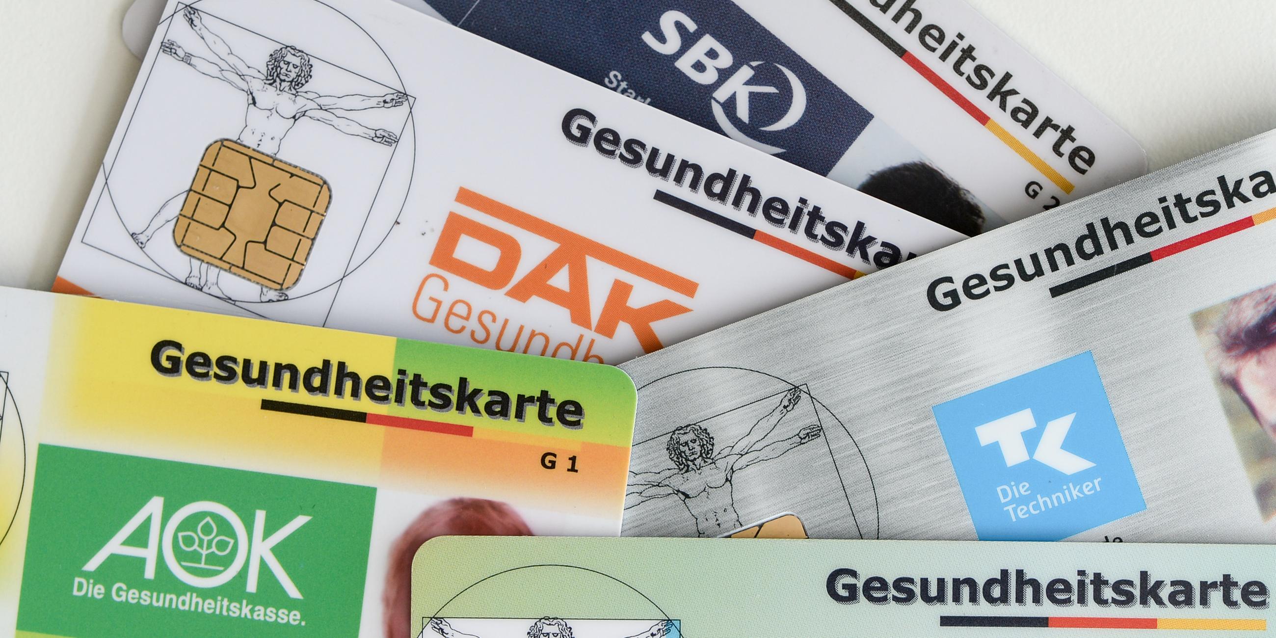 Gesundheitskarten verschiedener Krankenkassen liegen auf einem Tisch.