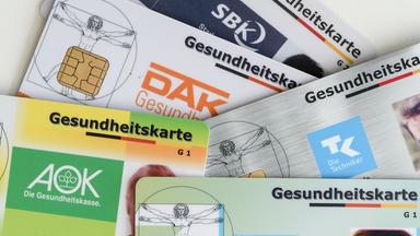 Gesundheitskarten verschiedener Krankenkassen liegen auf einem Tisch.