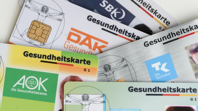 Gesundheitskarten verschiedener Krankenkassen liegen auf einem Tisch.