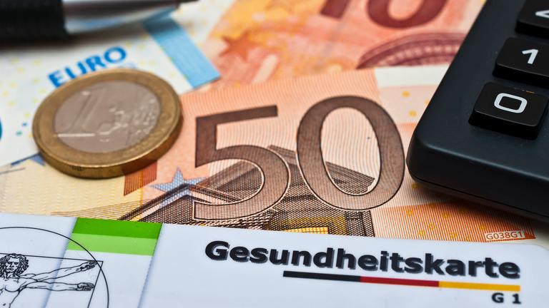 Krankenversicherungskarten, Geld und Taschenrechner liegen auf einem Tisch.