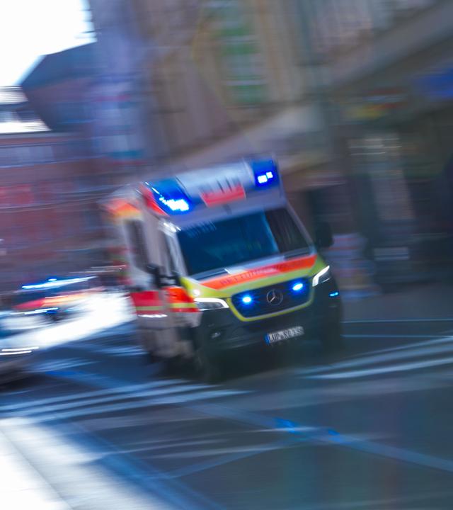 Ein Rettungsfahrzeug ist mit Blaulicht auf einer Straße unterwegs.