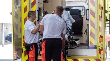 Rettungssanitäter heben an der Notaufnahme der Medizinischen Universität Lausitz eine Trage mit einer Patientin aus ihrem Rettungswagen.
