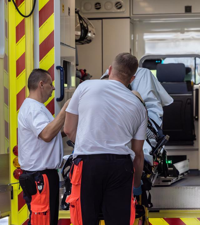 Rettungssanitäter heben an der Notaufnahme der Medizinischen Universität Lausitz eine Trage mit einer Patientin aus ihrem Rettungswagen.