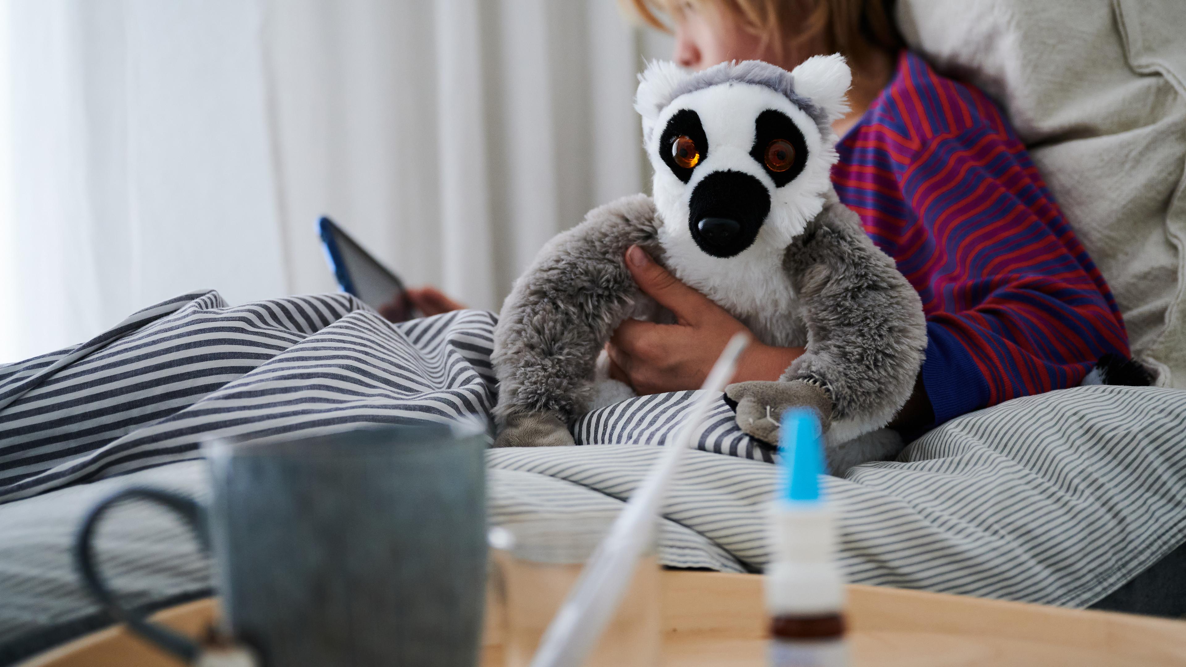 Krankes Kind liegt mit Stofftier im Bett