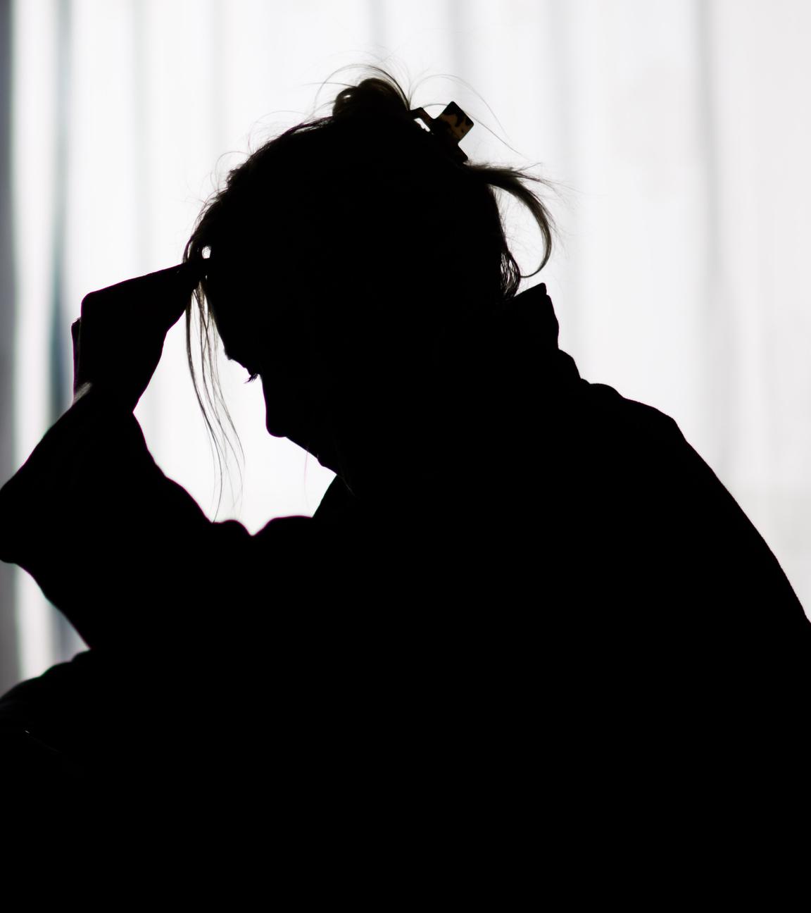 Die Silhouette einer Frau zeichnet sich vor einer hellen Fensterfront ab.