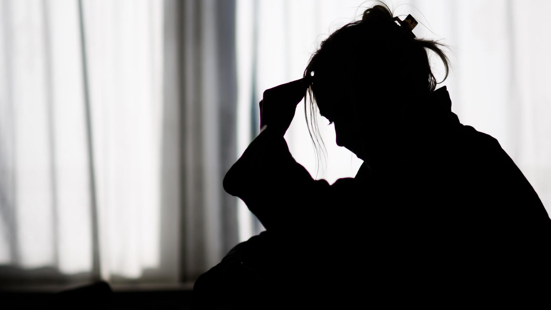 Die Silhouette einer Frau zeichnet sich vor einer hellen Fensterfront ab.