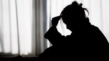 Die Silhouette einer Frau zeichnet sich vor einer hellen Fensterfront ab.