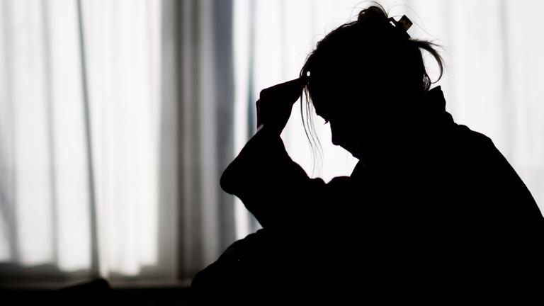 Die Silhouette einer Frau zeichnet sich vor einer hellen Fensterfront ab.