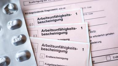 Mehrere Formulare zur Arbeitsunfähigkeitsbescheinigung liegen neben einem Blister mit Tabletten auf einem Tisch.