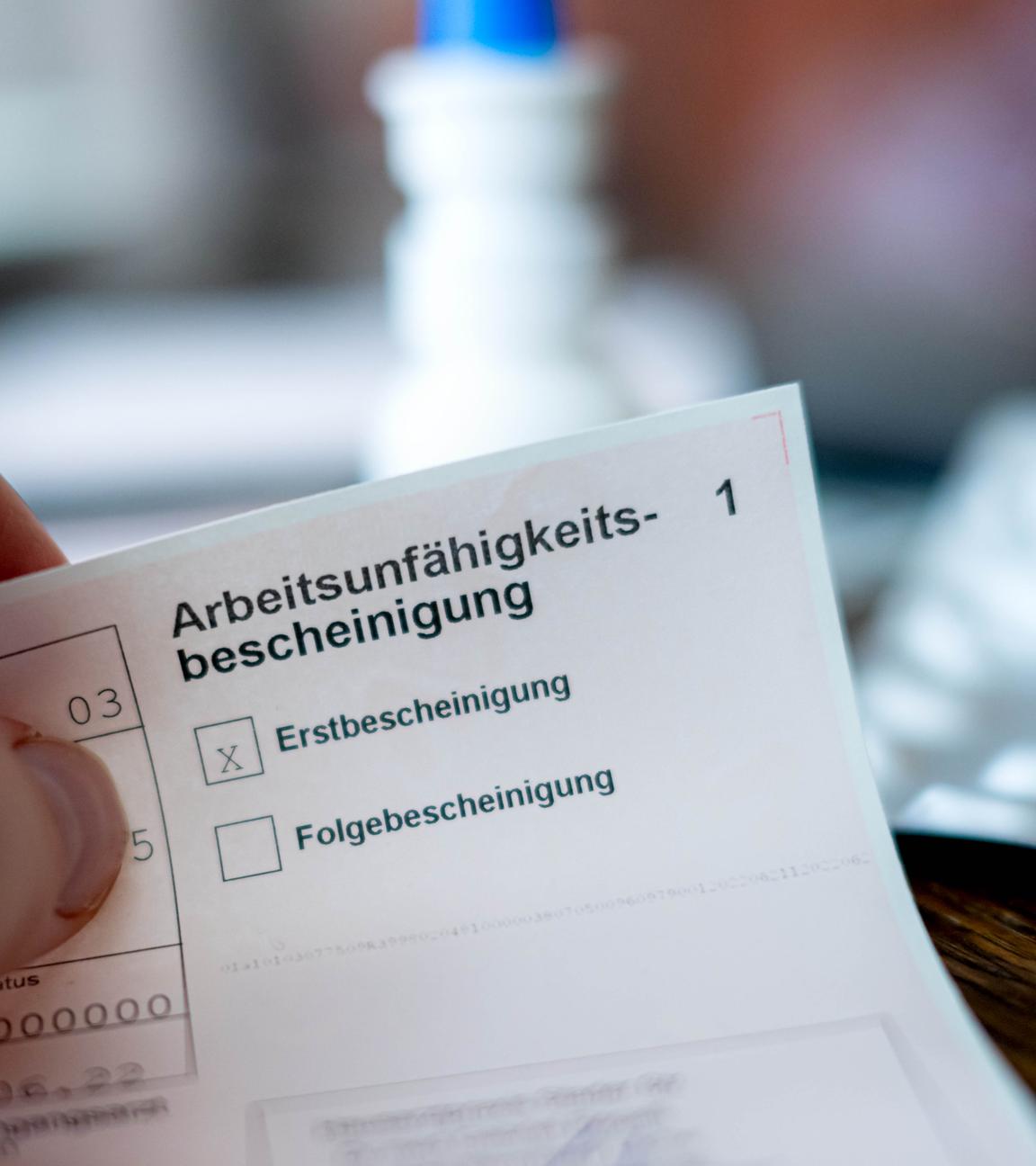 Eine Person hält eine ausgefüllte Arbeitsunfähigkeitsbescheinigung in der Hand