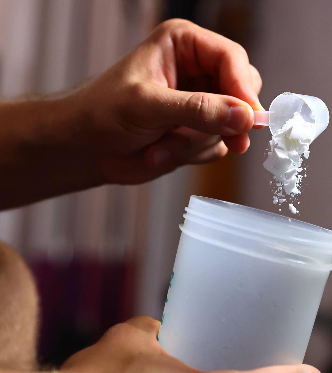 Mann füllt Kreatinpulver in einen Trinkbecher.