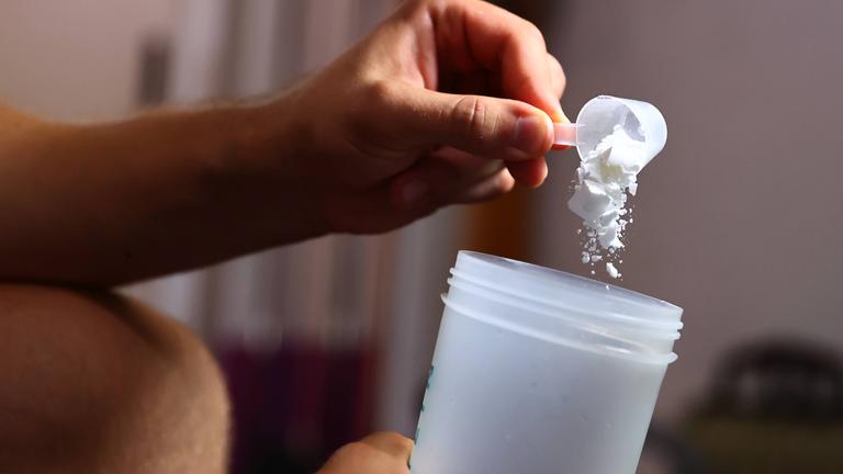Mann füllt Kreatinpulver in einen Trinkbecher.