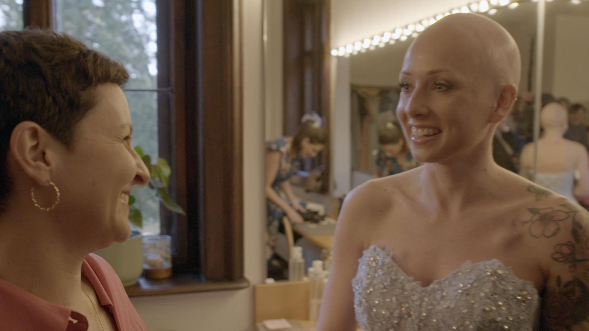 Die an Brustkrebs erkrankte Vanessa Schmidt (rechts) trägt ein glitzerndes Kleid. Sie unterhält sich mit Susanne Honig (links). Beide lachen.