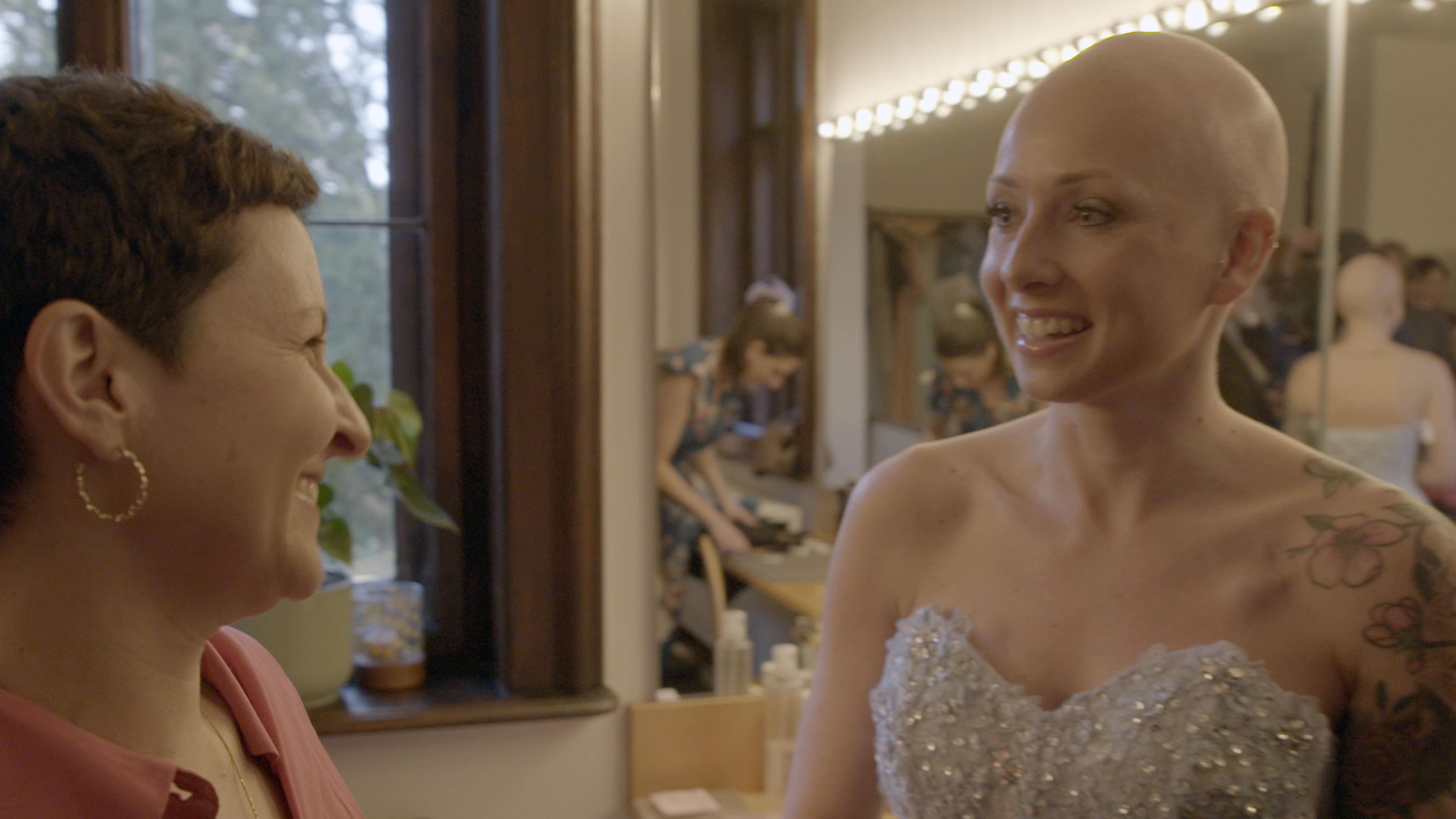 Die an Brustkrebs erkrankte Vanessa Schmidt (rechts) trägt ein glitzerndes Kleid. Sie unterhält sich mit Susanne Honig (links). Beide lachen.