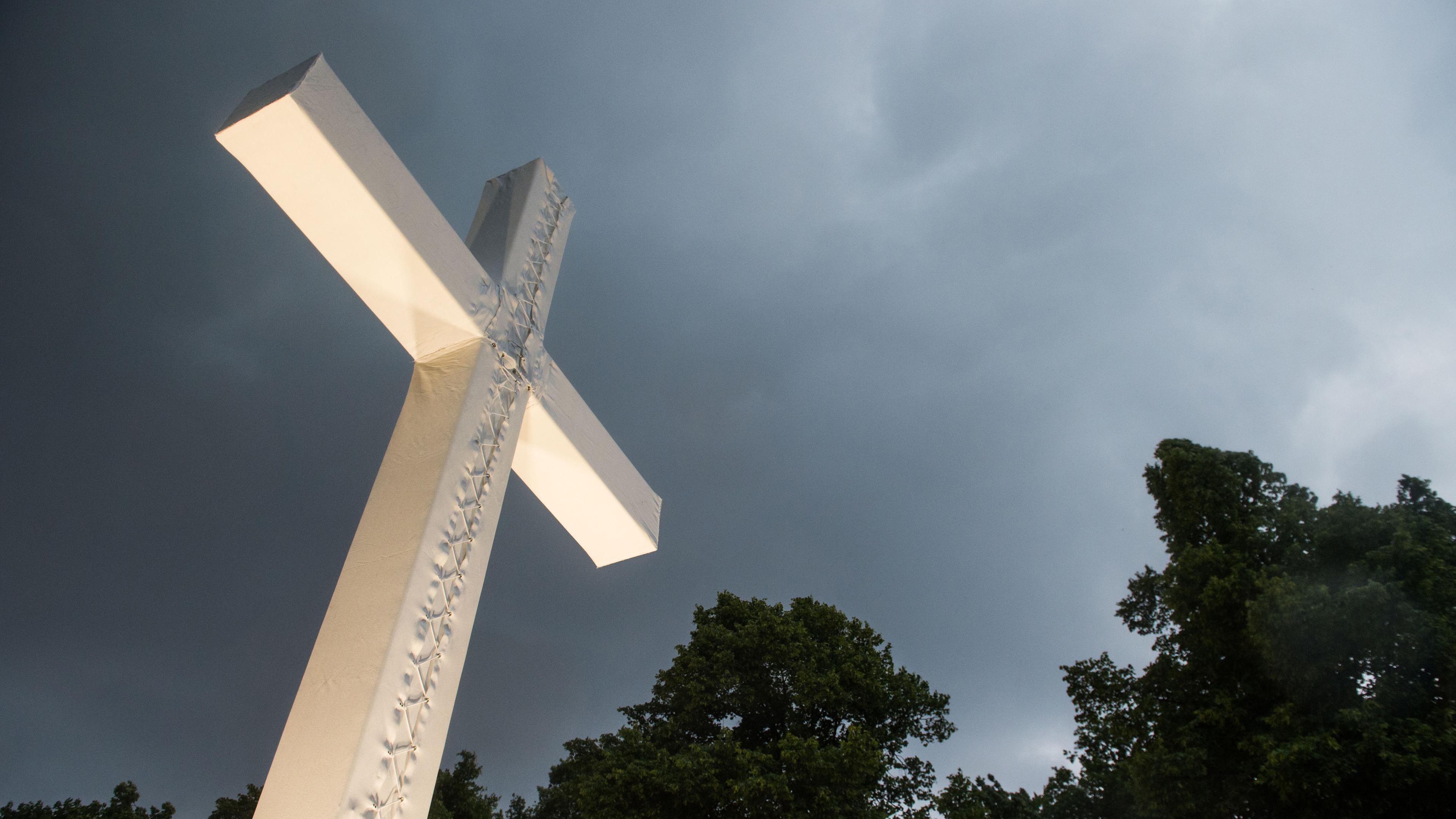Berlin: Dunkle Wolken ziehen über einem überdimensionierten Kreuz auf.