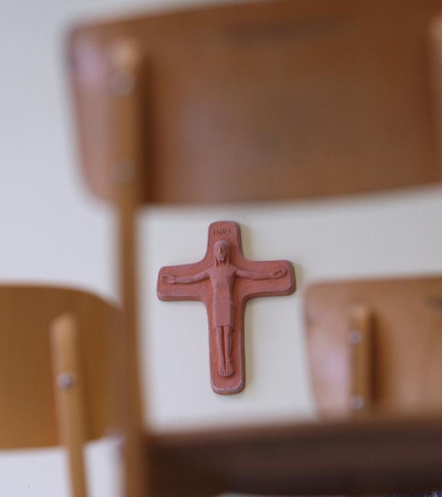 Ein Kreuz hängt in einem Klassenzimmer der Grundschule in Kaufbeuren, Schwaben, hinter auf Schulbänken gestellten Stühle am 27.04.2010. 