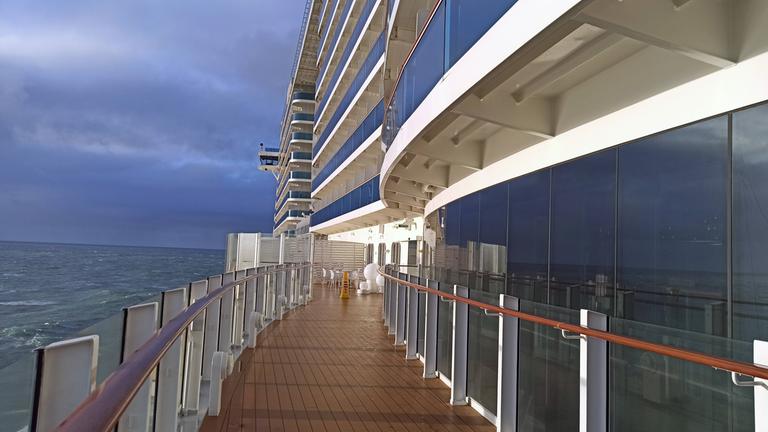 Ein Gang auf dem Deck eines Kreuzfahrtschiffes und Kabinen darüber mit Blick auf das Meer.