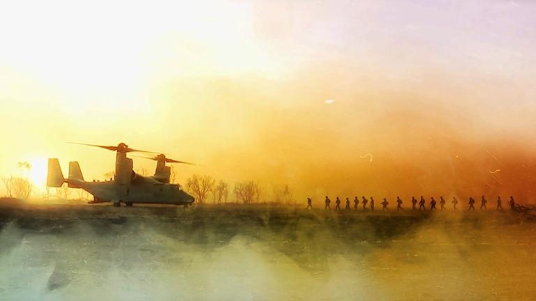 Ein Hubschrauber steht bei Sonnenuntergang auf einem freien Feld. Mehrere Soldaten laufen auf den Hubschrauber zu.