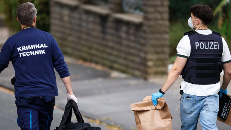 Mitarbeiter der Kriminalpolizei laufen eine Straße entlang. In Menden wurde ein Mann am 22.08.2025 durch Schüsse getötet und ein weiterer verletzt.