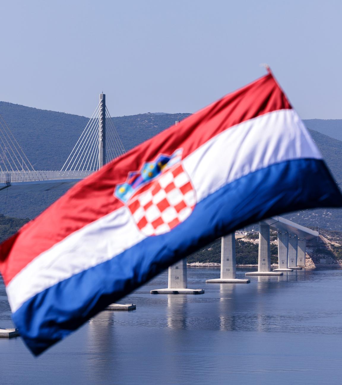 Kroatische Flagge weht im Wind, im Hintergrund ist die Peljesac-Brücke