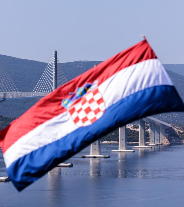 Kroatische Flagge weht im Wind, im Hintergrund ist die Peljesac-Brücke
