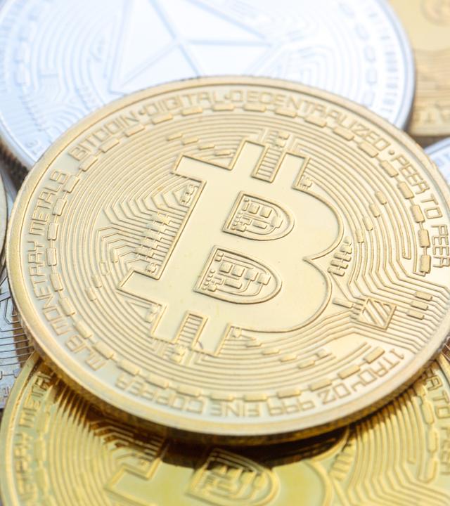 Münzen mit den Symbolen von Bitcoin (M) und Ethereum sind auf einem Tisch angeordnet. 