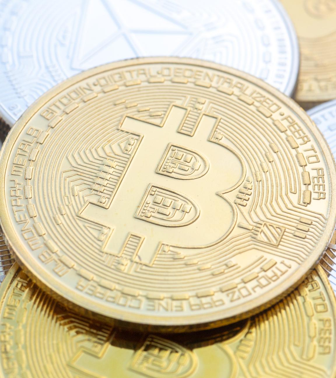 Münzen mit den Symbolen von Bitcoin (M) und Ethereum sind auf einem Tisch angeordnet.