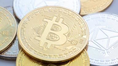 Münzen mit den Symbolen von Bitcoin (M) und Ethereum sind auf einem Tisch angeordnet.